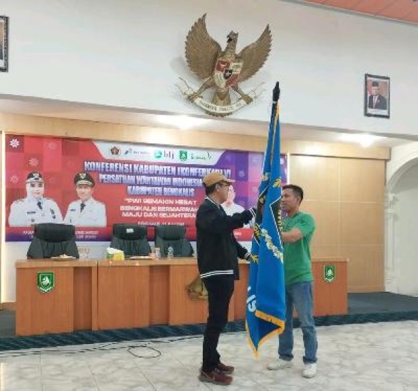 Ketua PWI Riau Raja Isyam Azwar menyerahkan pataka kepada Adi Putra, usai terpilih aklamasi di Konferkab VI PWI Bengkalis, Selasa (23/7/2024). (istimewa)