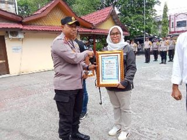 Kapolres Siak AKBP Asep Sujarwadi menyerahkan penghargaan kepada Ketua PWI Siak, Wiwik Widianingsih, Senin (6/1/2025) di halaman Mapolres Siak. (istimewa)